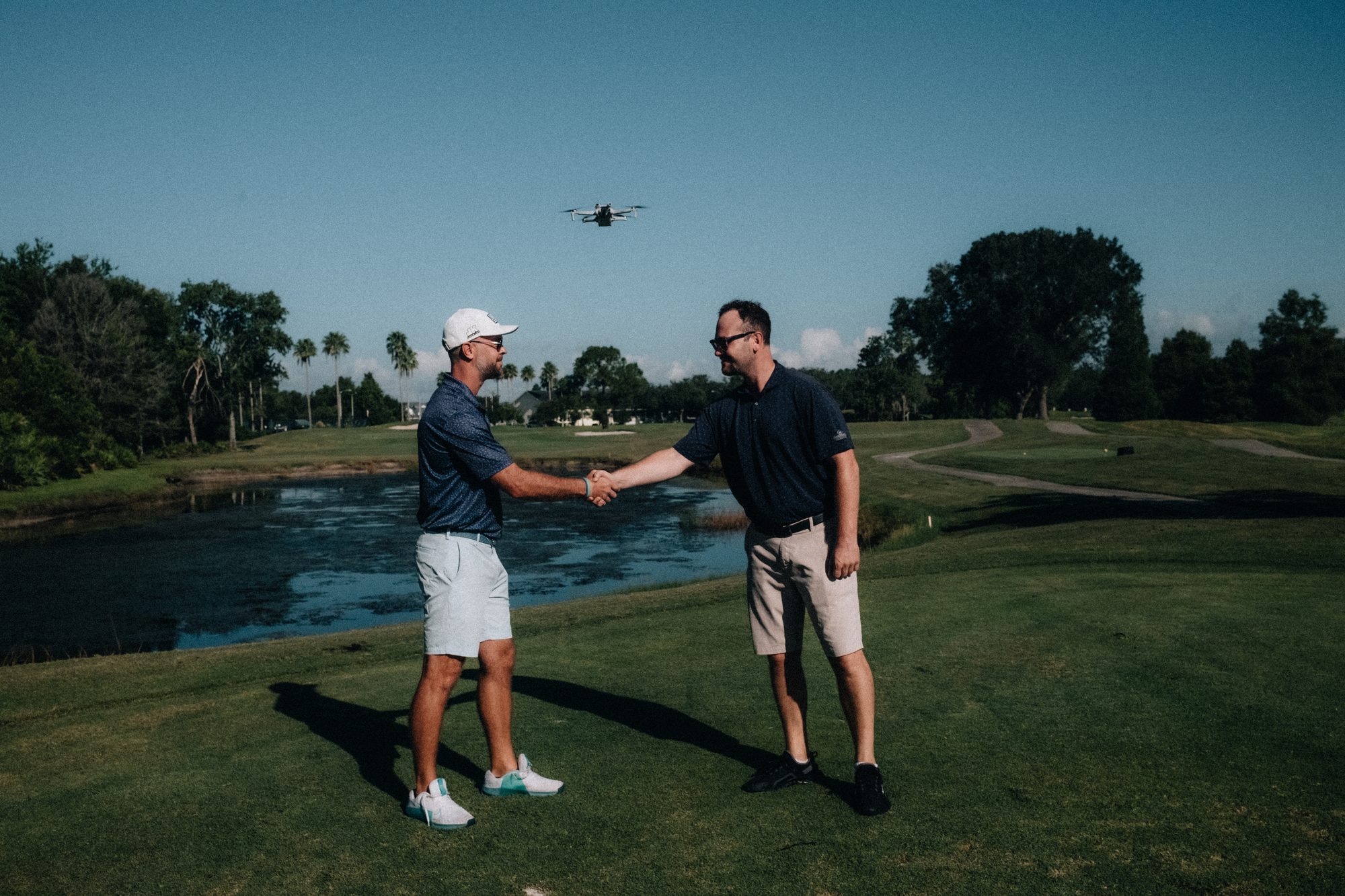 Two men shaking hands on a golf course with a drone overhead