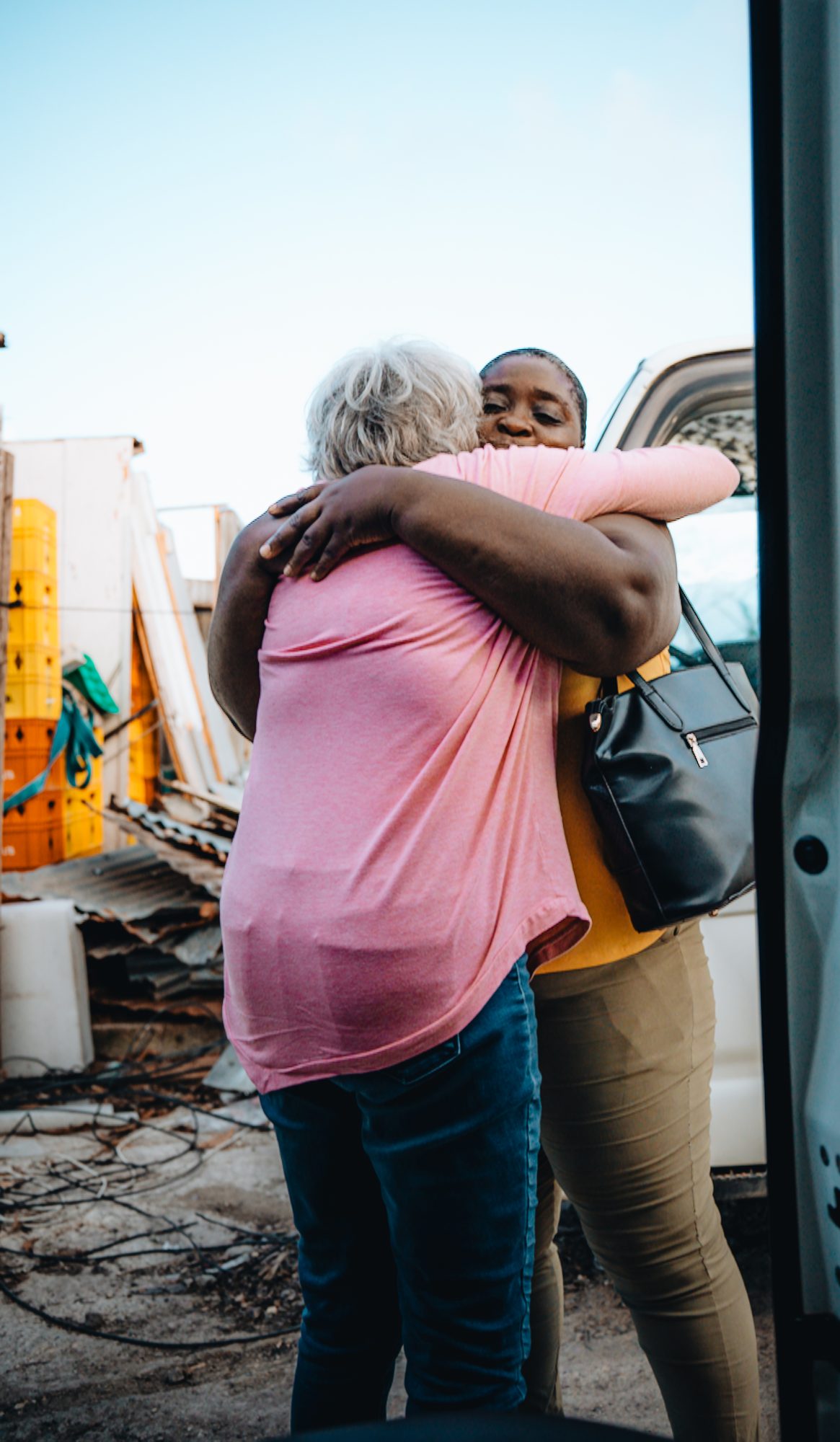 Two women hugging next to a car full of supplies