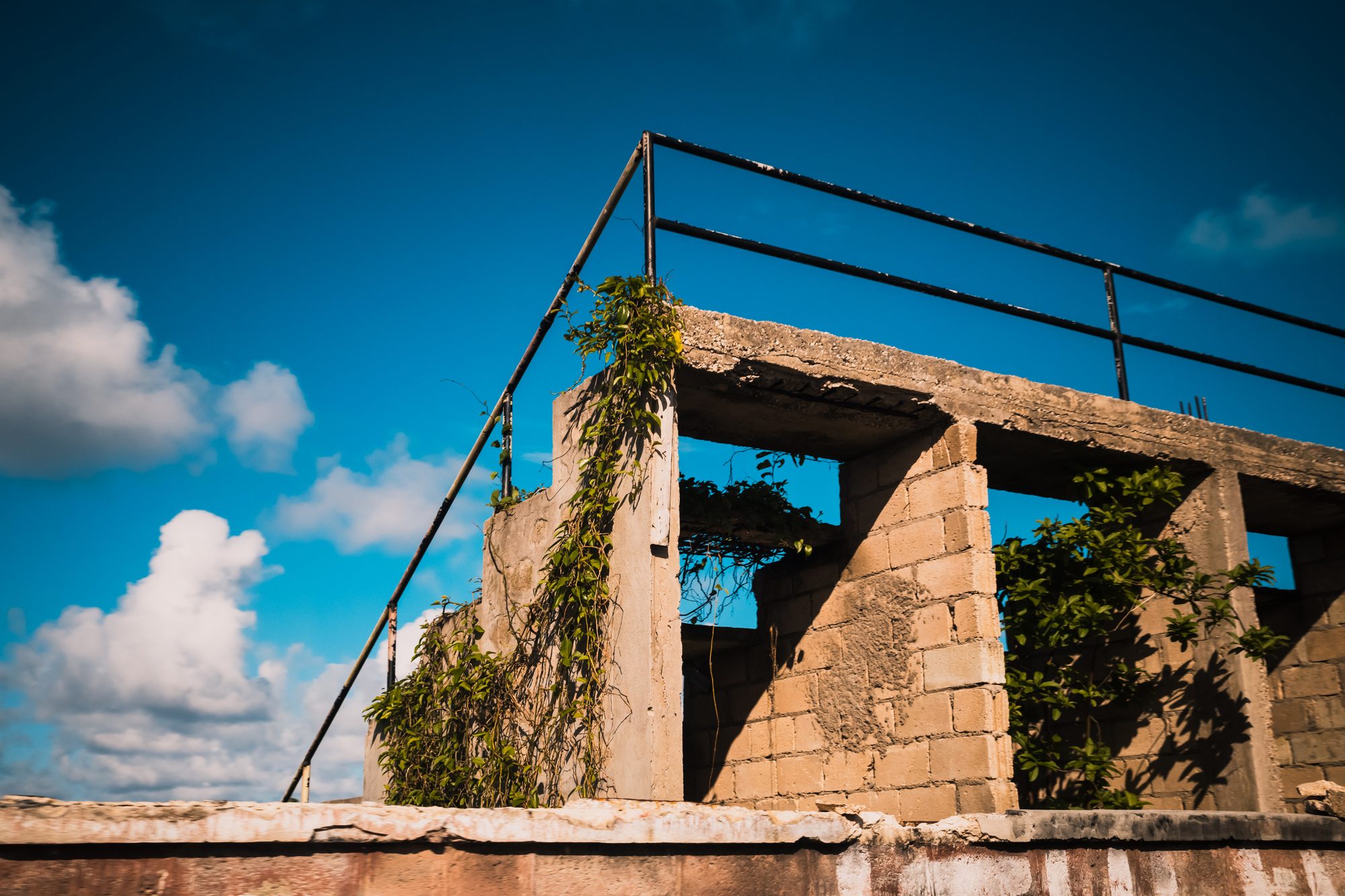 Concrete house with its roof gone, rebar against a blue sky