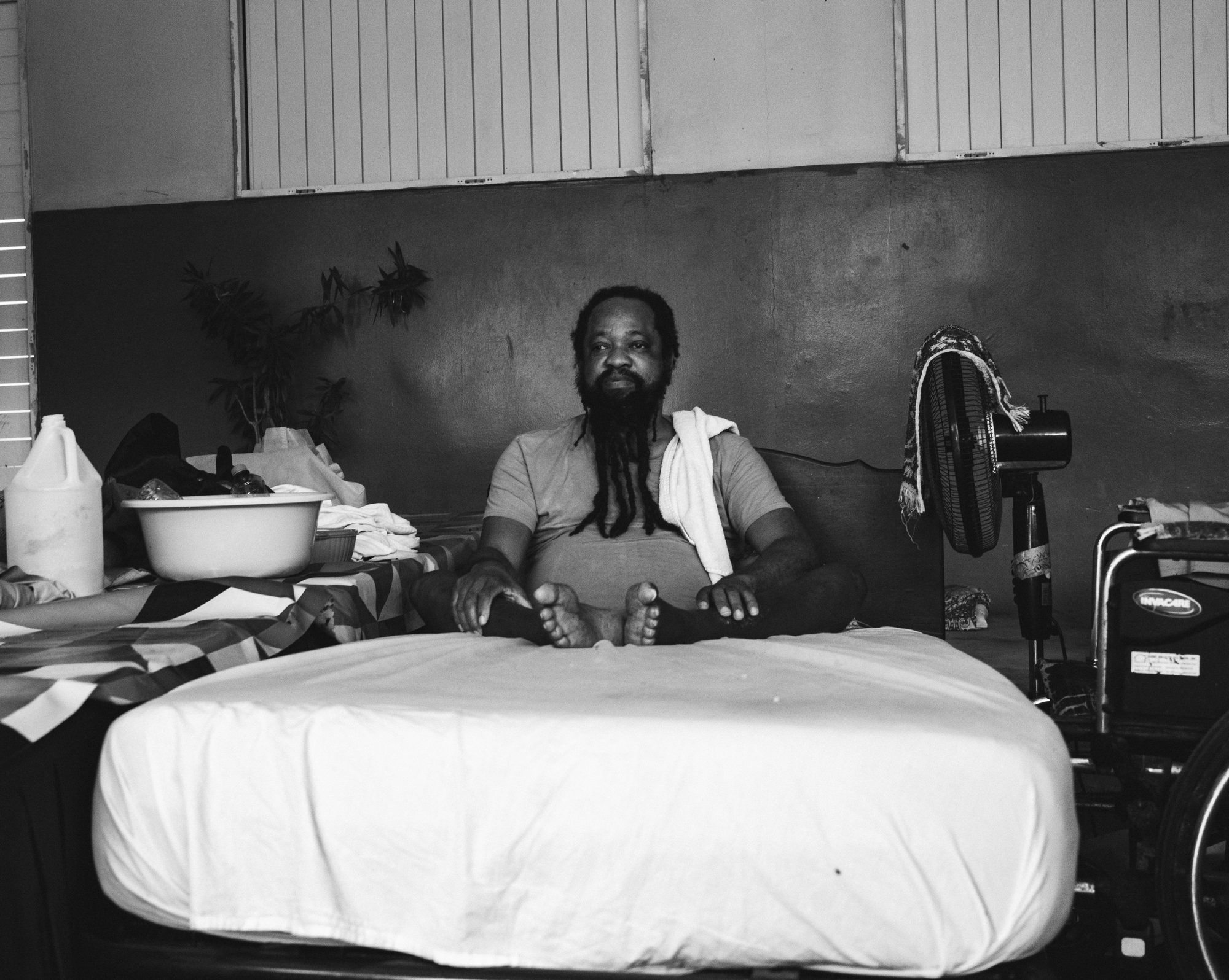 Man sitting on a bare mattress in a shelter, black and white