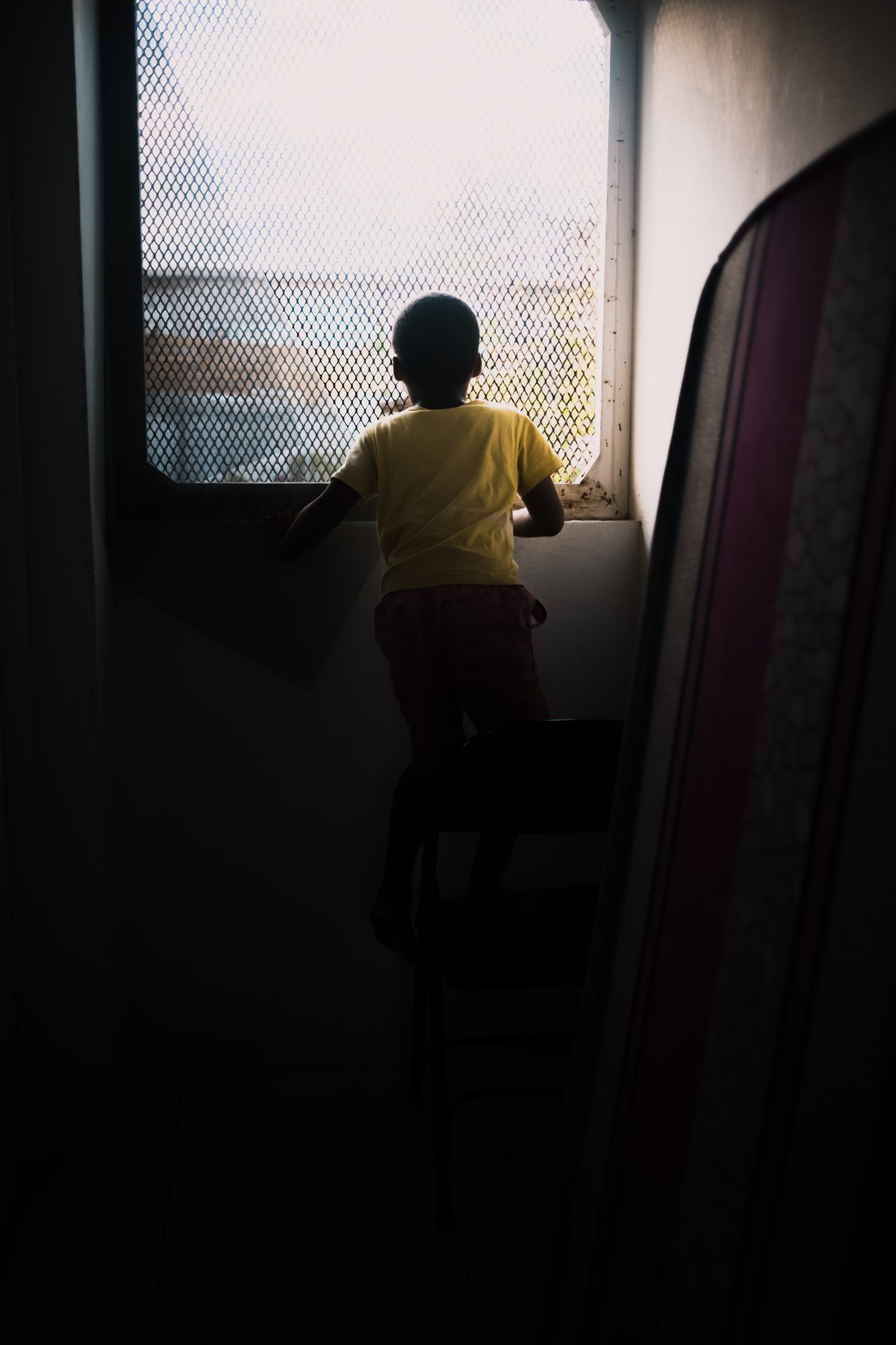 Child at a window, seen from a dark room
