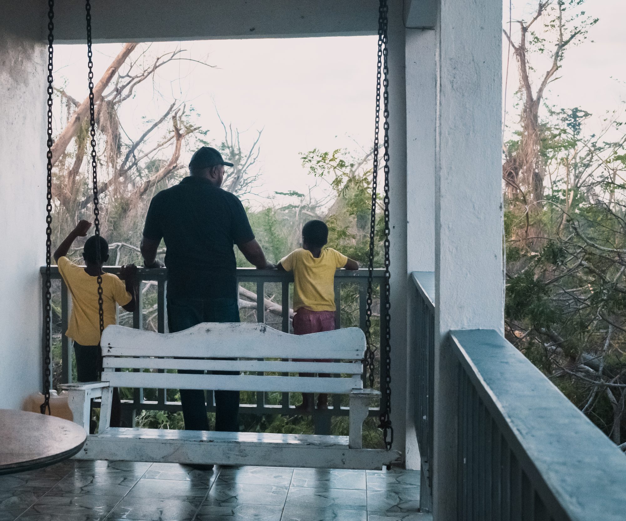 A man and two children on a porch looking out at stripped trees