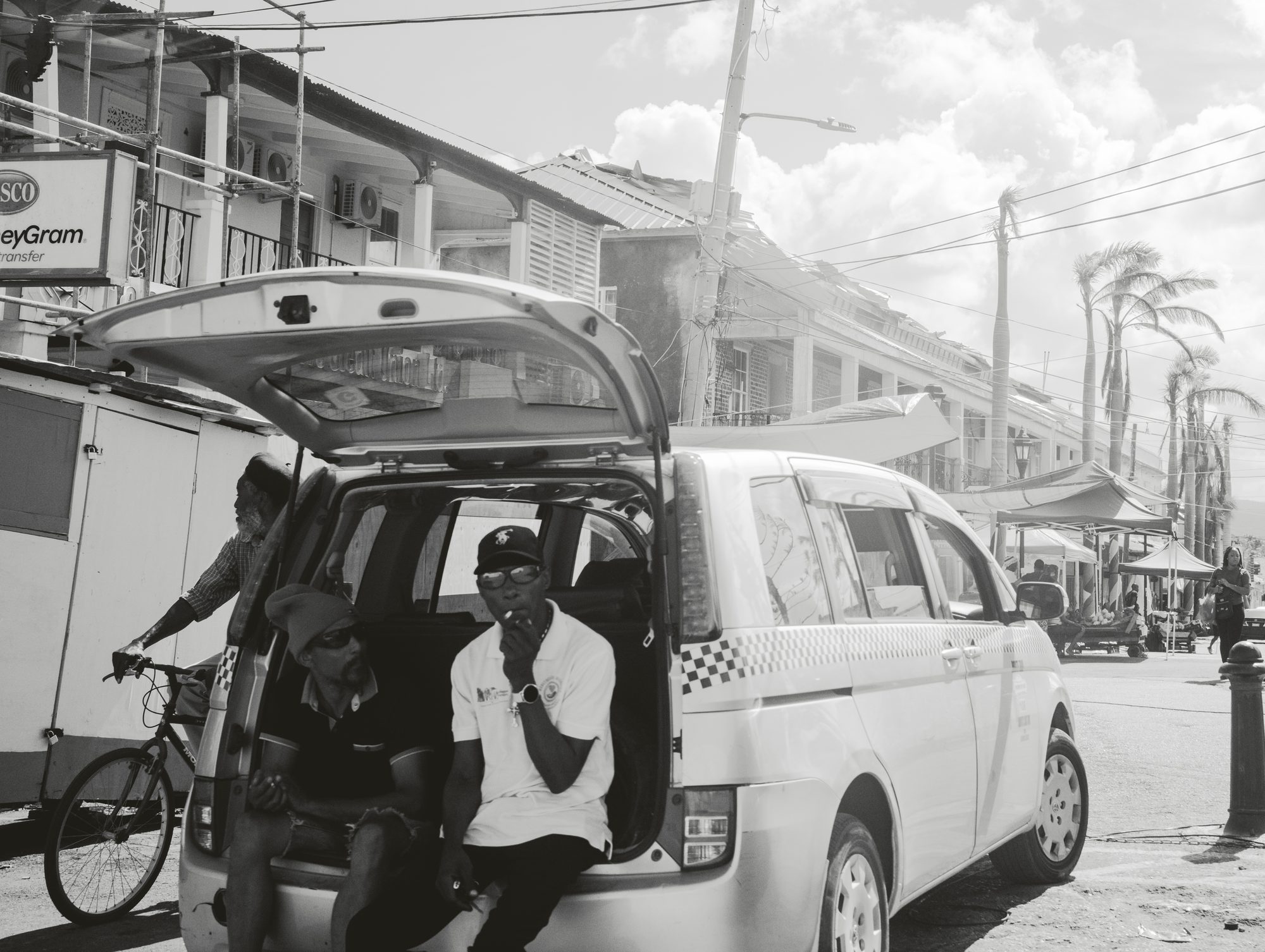People unloading a car on a town street, black and white