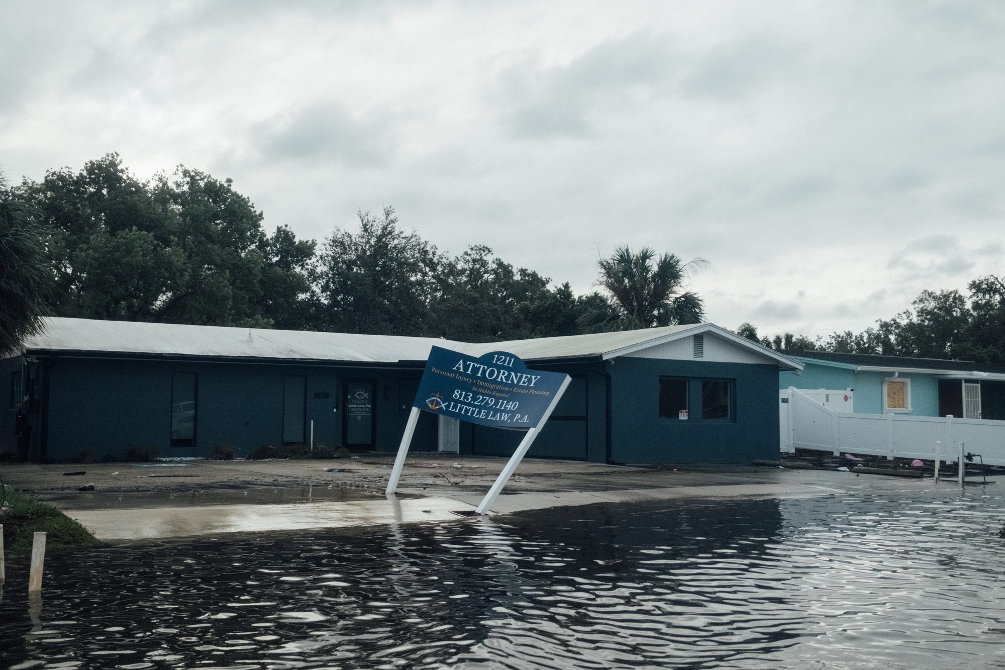 Office building standing in floodwater, its sign knocked sideways