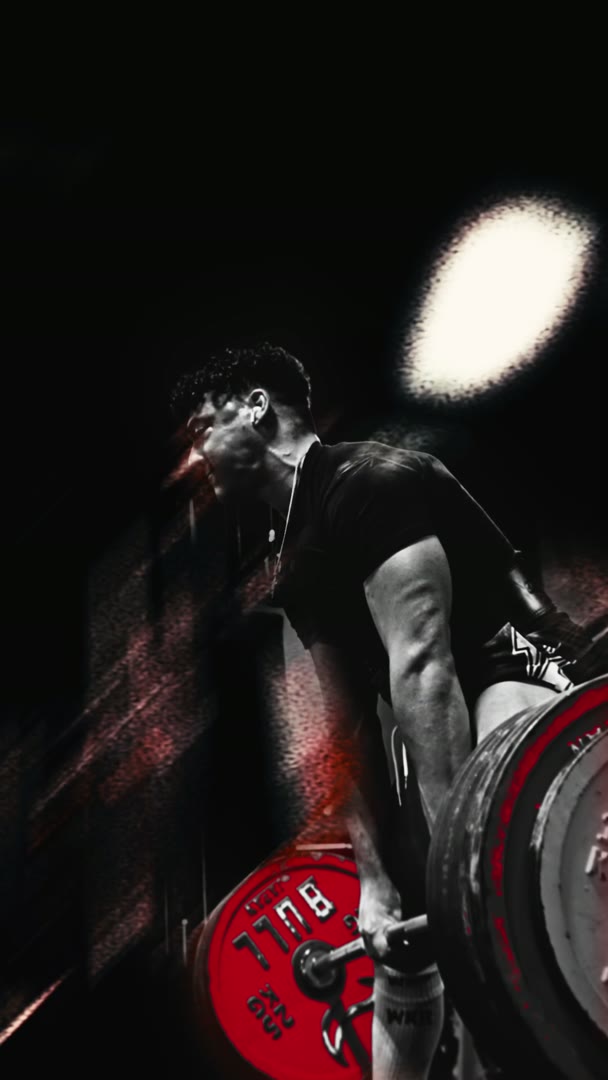 A lifter pulling a loaded barbell, shot in black and white with the red plates left in colour